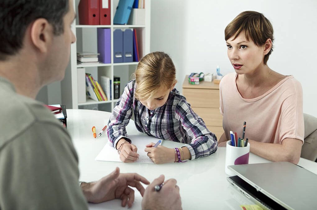 Mother speaking with a man at a desk while child draws on paper