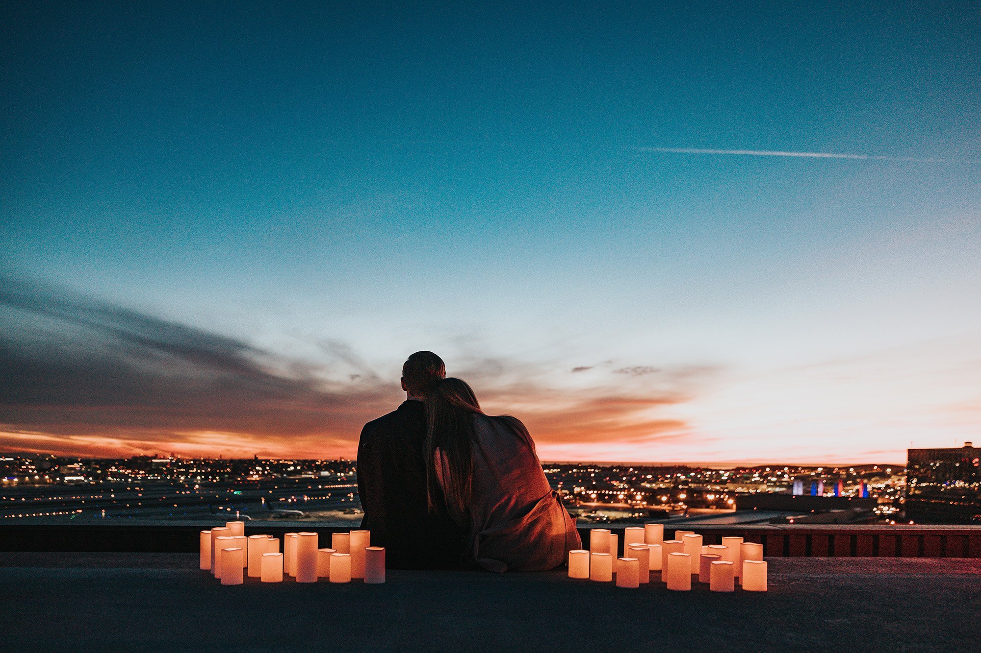 Man and woman sitting around candles watching the sunset.