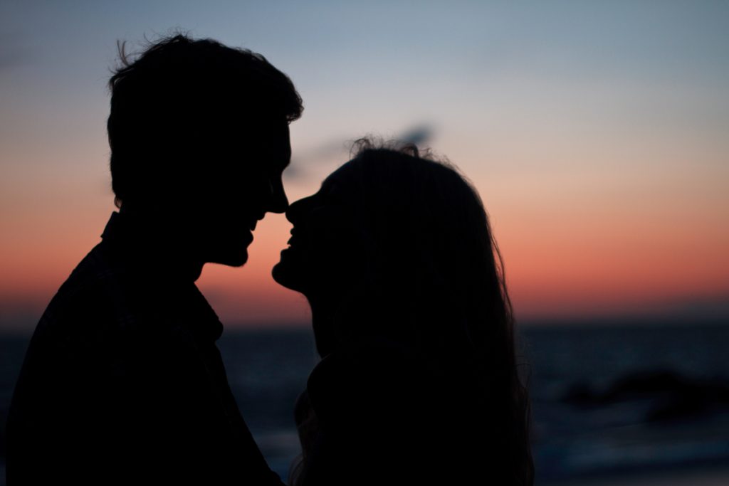 Man and women touching noses in front of a sunset
