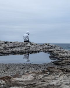 Teen with a hood on sitting alone on a rock near a beach