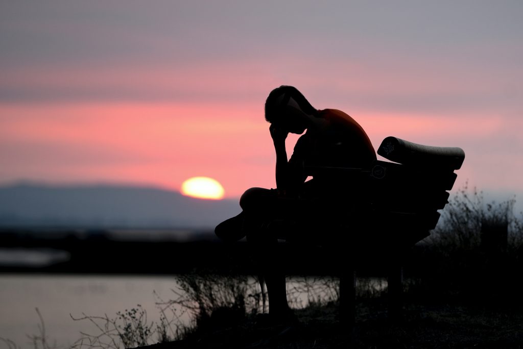 man sitting on a bench at sunset with his hand on his head