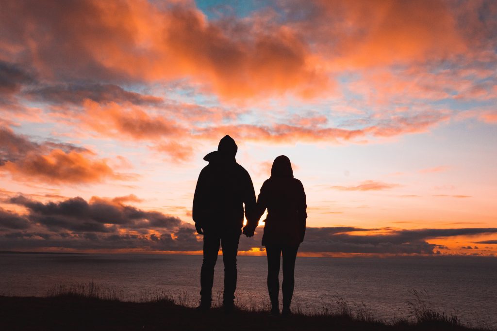couple holding hands and looking at the sunset and colors of the sky