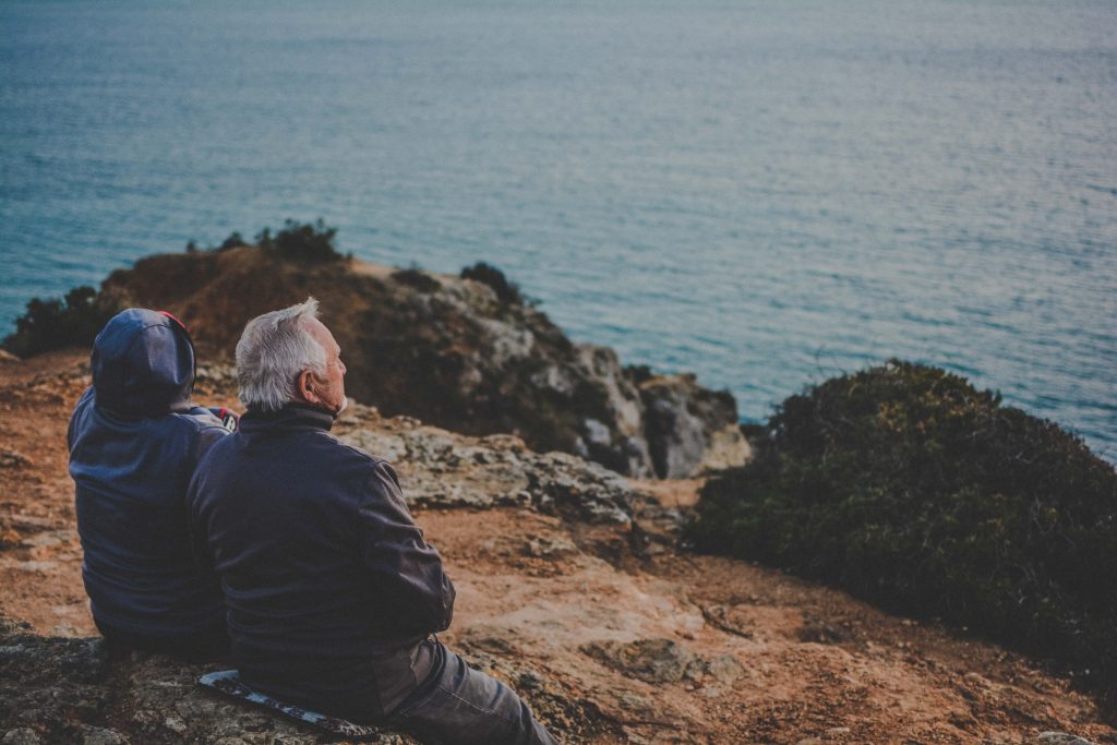 elderly couple sitting on the rocks and looking at the water