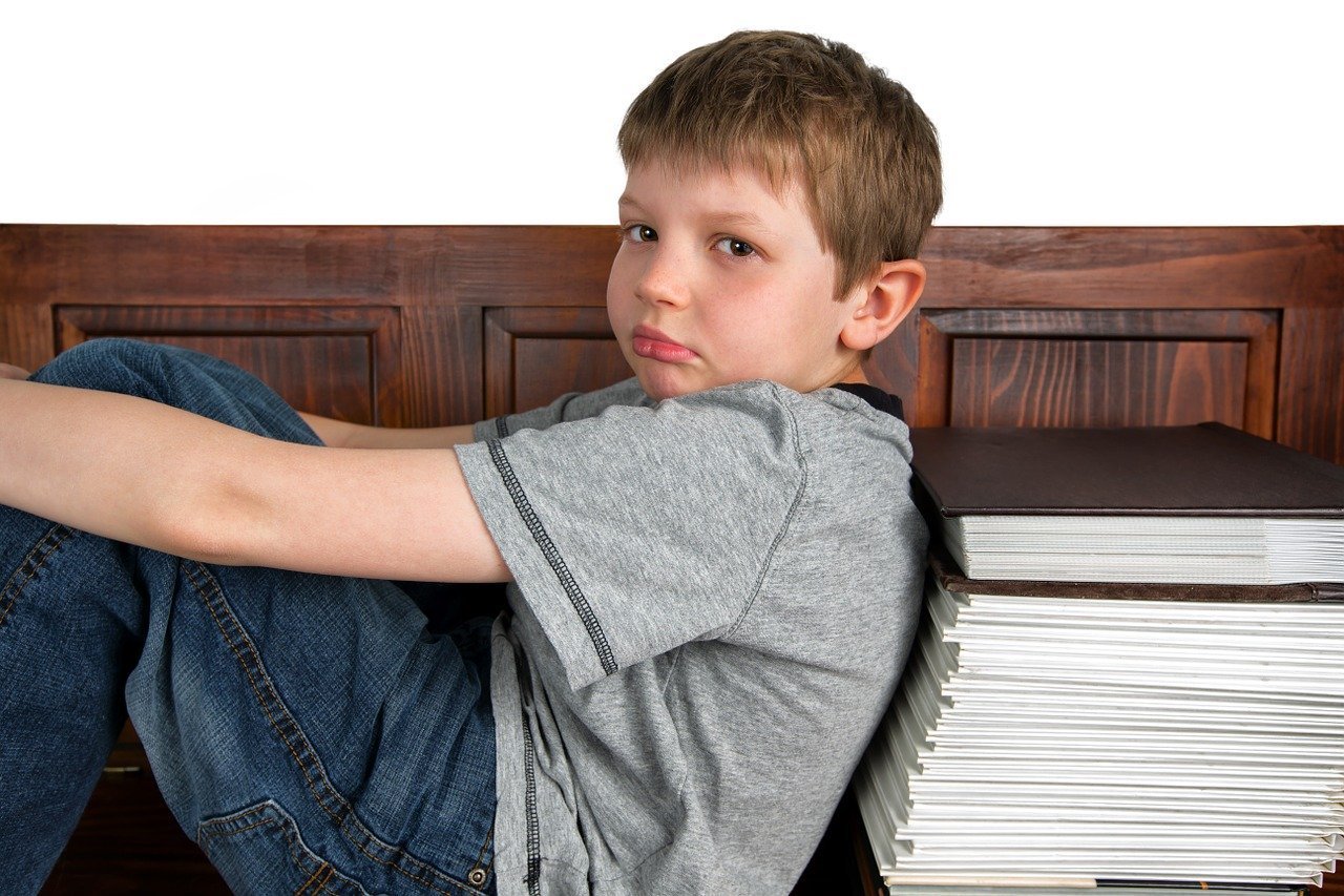 boy sitting against a large stack of books with an expression of sadness