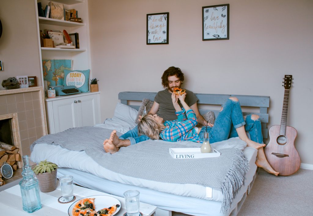couple eating pizza together in a bed room