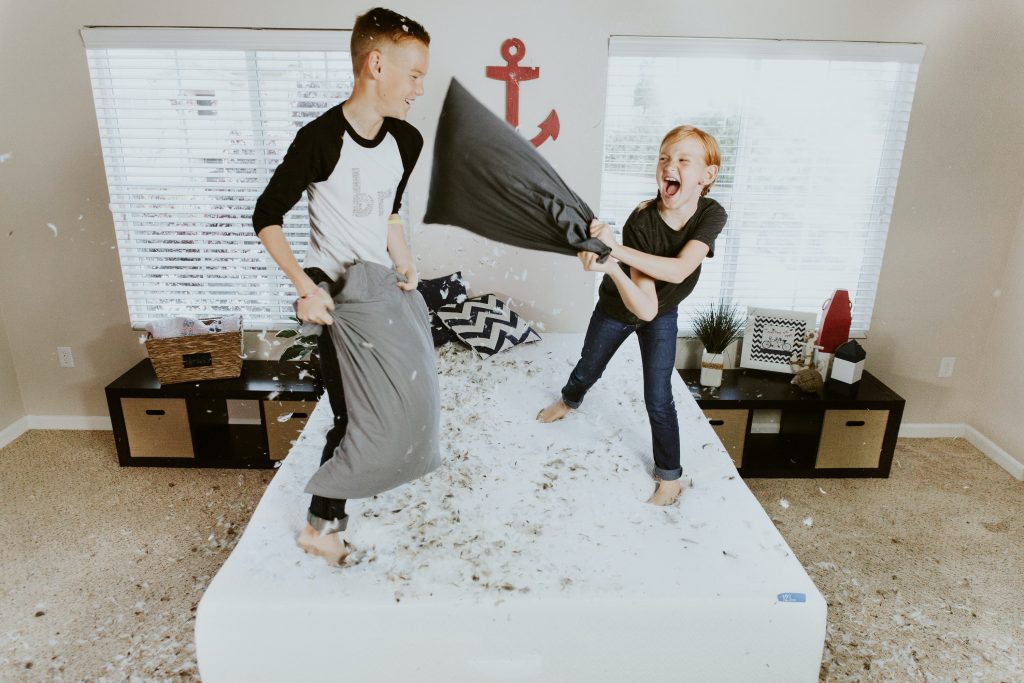 happy kids having a pillow fight standing on top of a bed 