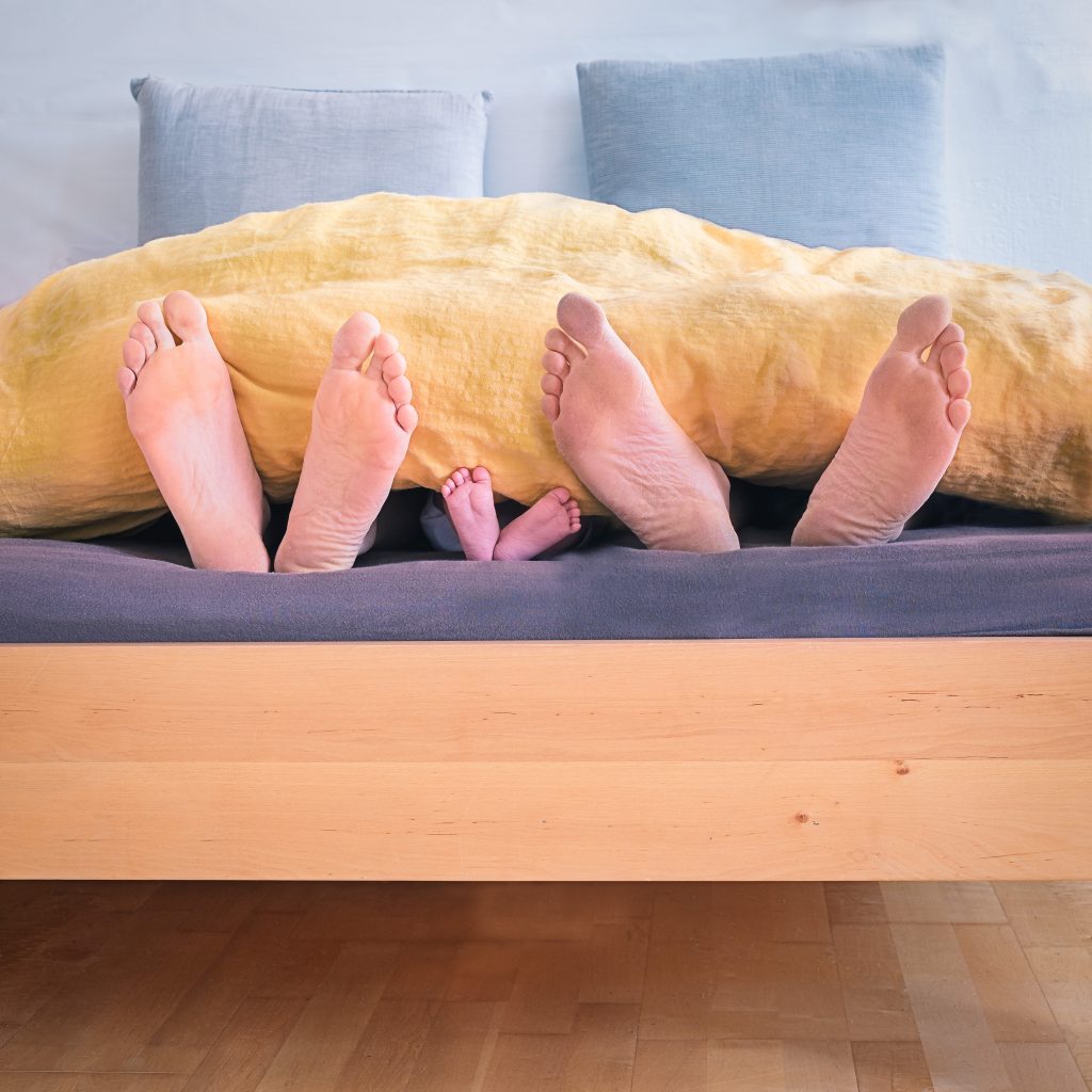 feet sticking out from under the covers of a bed. Two adults and one child in between them