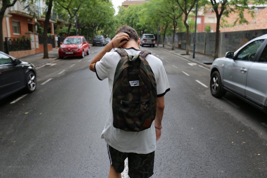 boy with backpack walking down a street with his hand on his head