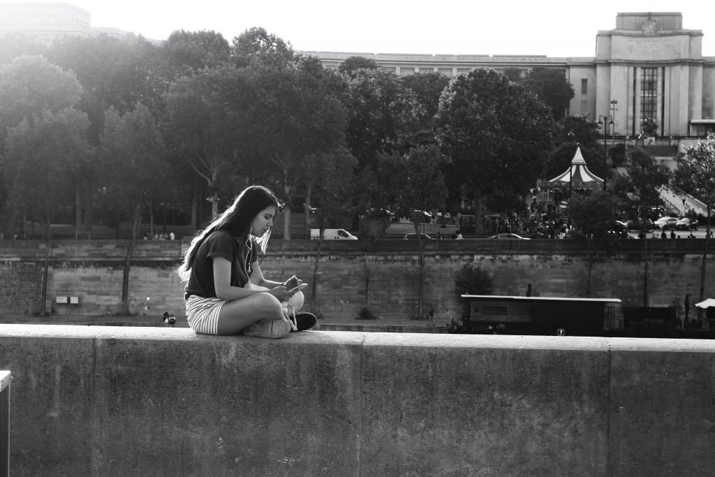 girl sitting on a cement wall using the headphones on her cellphone 