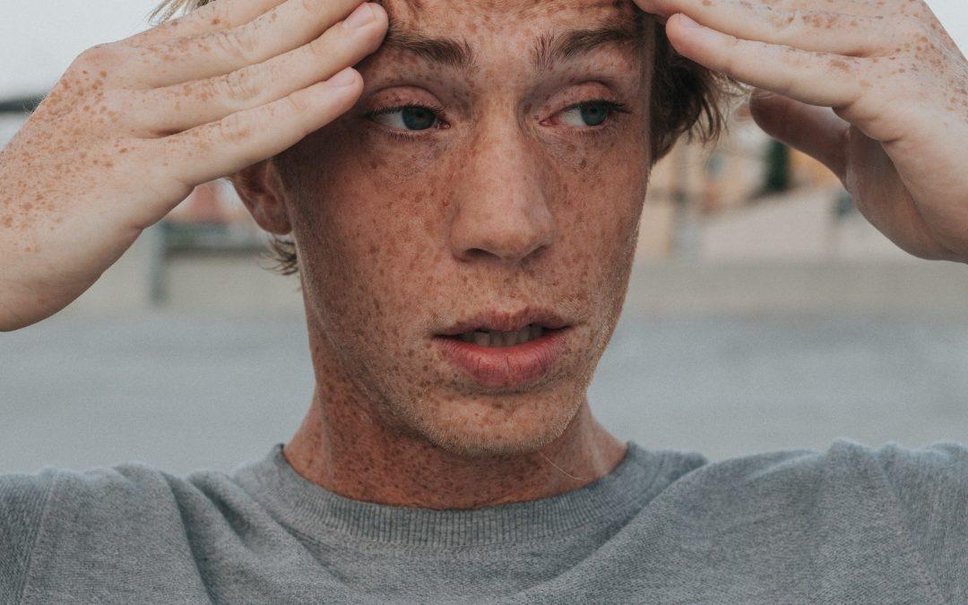 teen with freckles holding his head