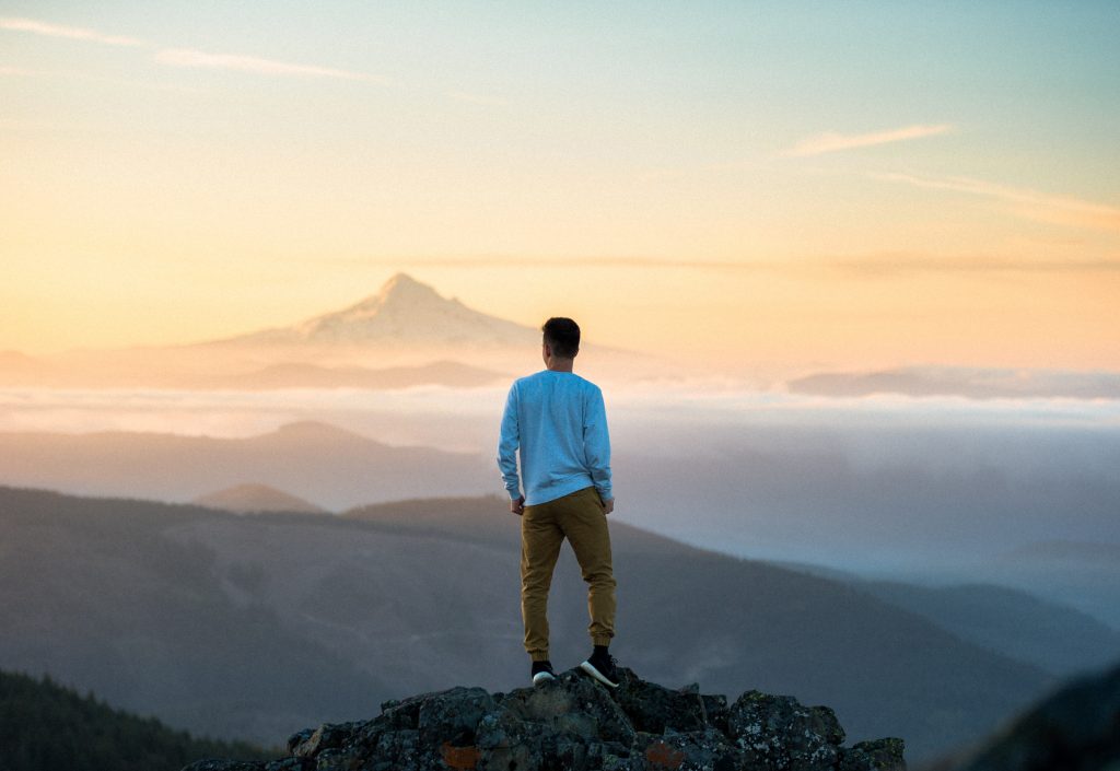 man standing on cliff and looking at the mountains far away