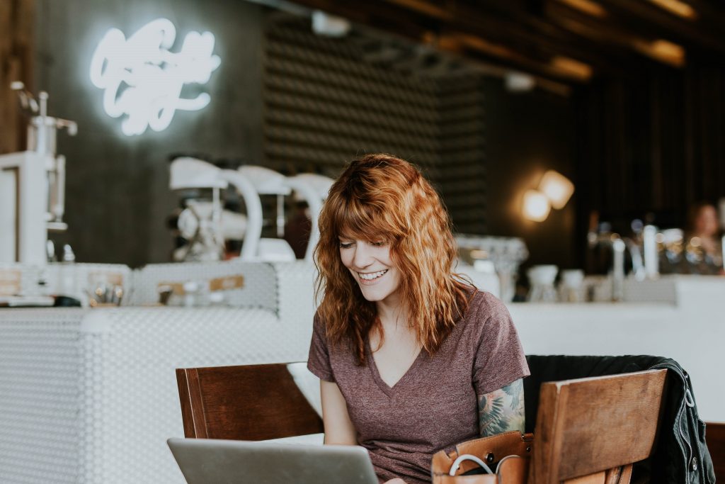 smiling woman with open hair sitting in a cafe and working on a laptop