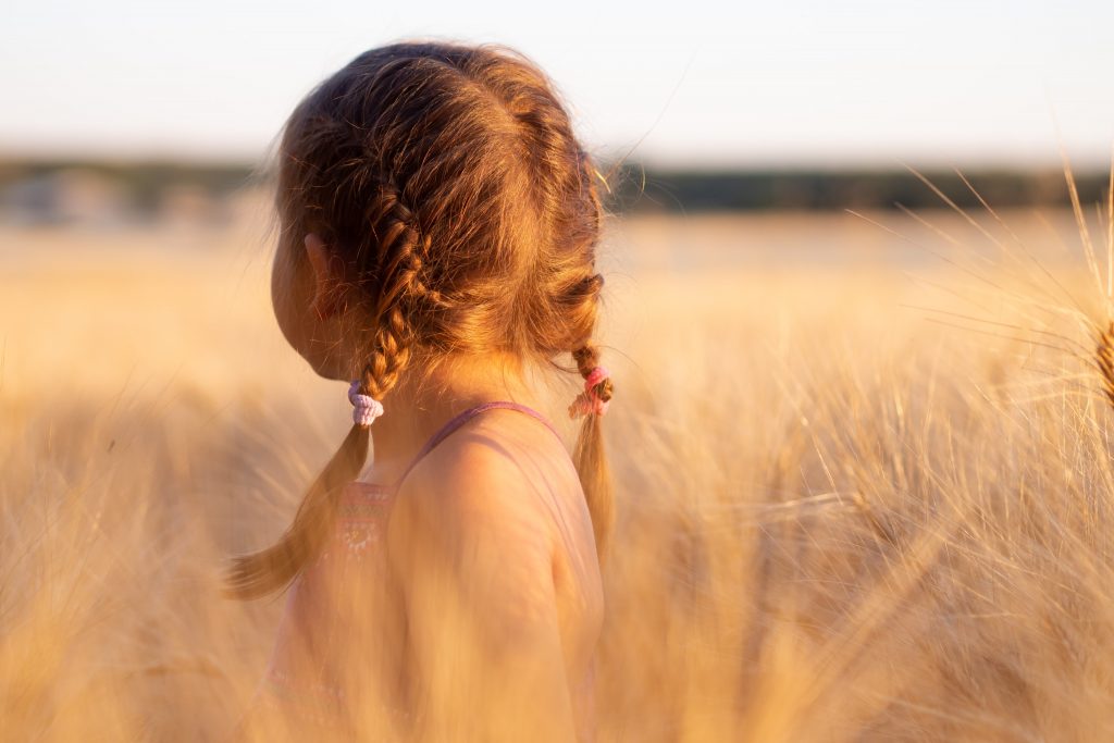 child with braided pigtails looks away in a feild 