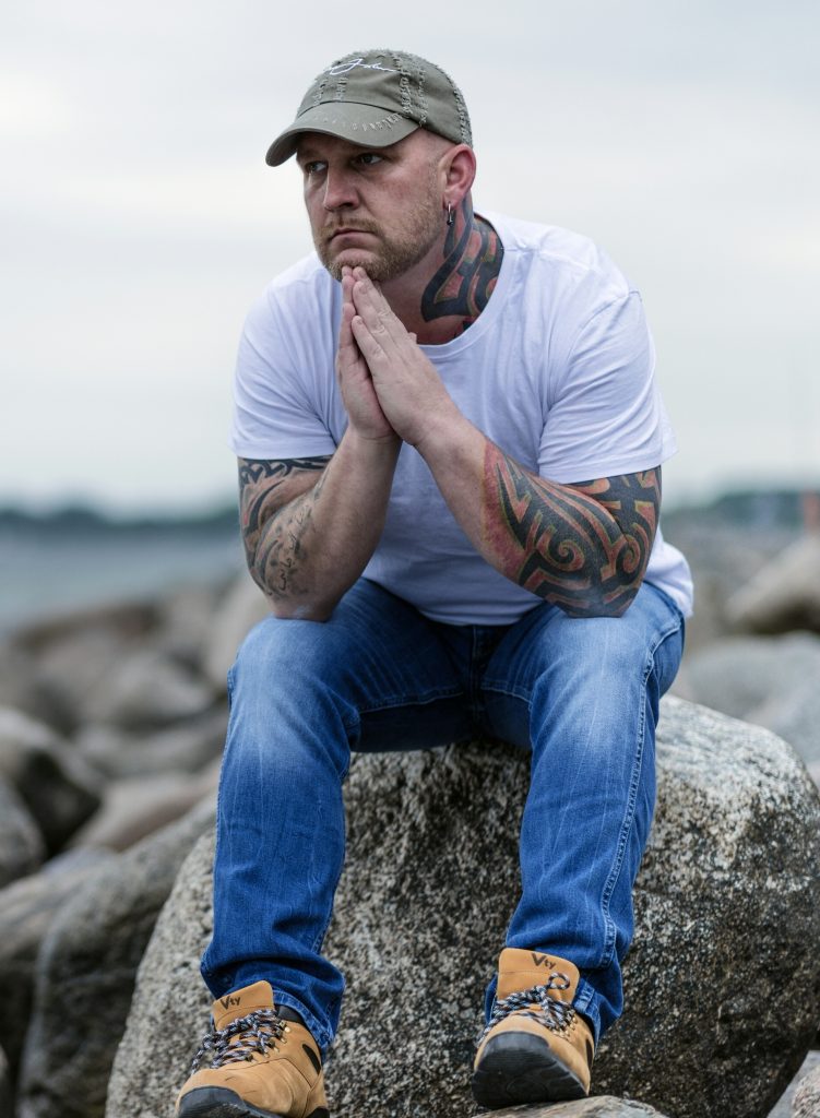 man with tattoos sitting on a rock holding his hands up to his face