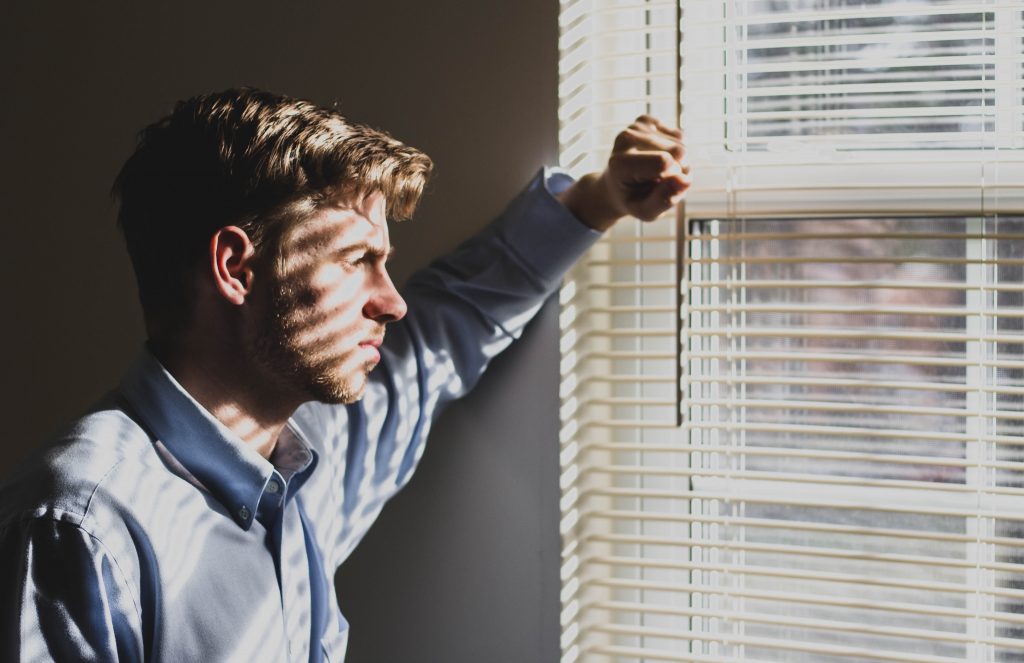 man looking out of a window with blings squinting 