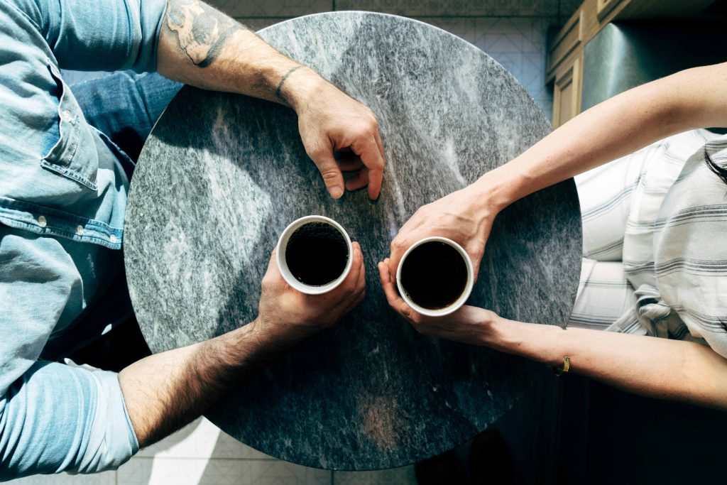 two people holding cups of black coffee at a blue round table
