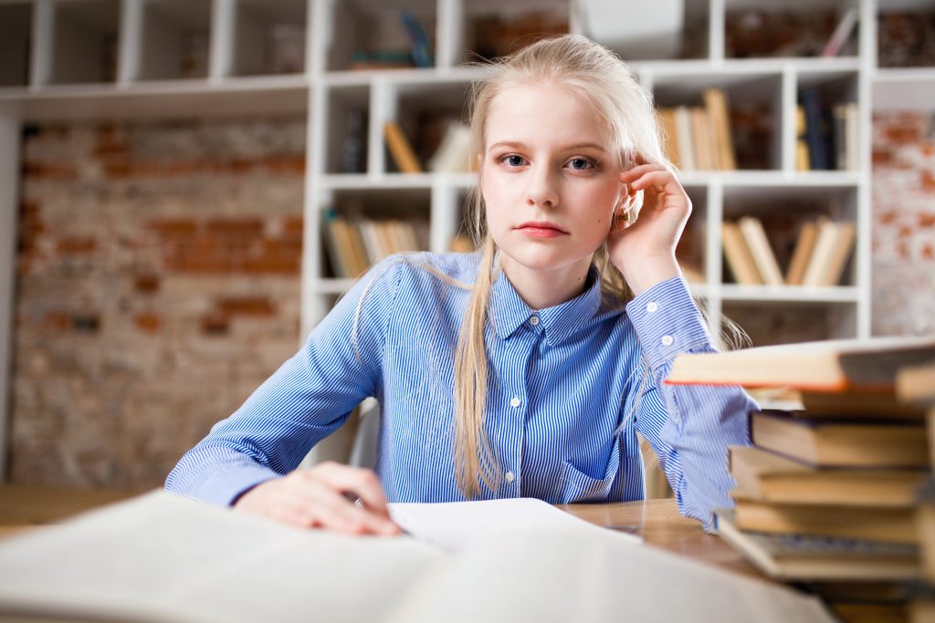 girl with blonde hair wearing a blue shirt sitting at a desk 