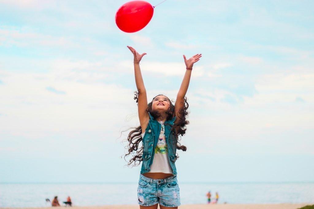 young girl with curly hair playing with a red balloon 