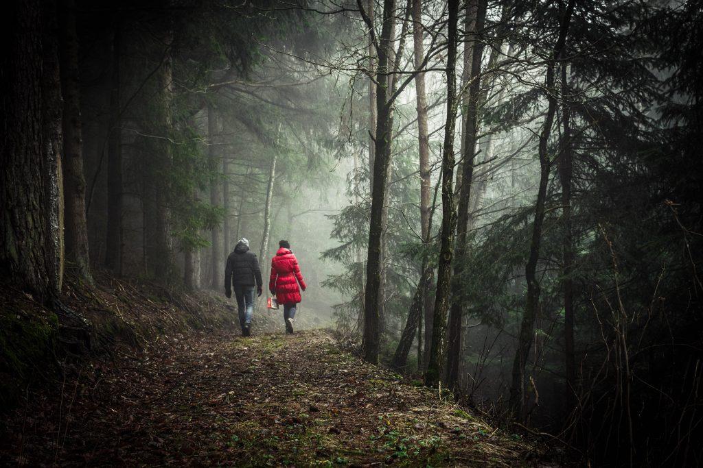 man and woman wearing coats walking through a forest 