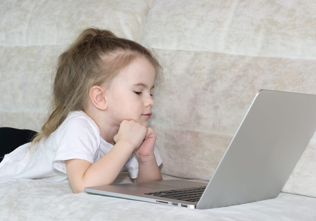 child with their hands holding their head up watching a laptop