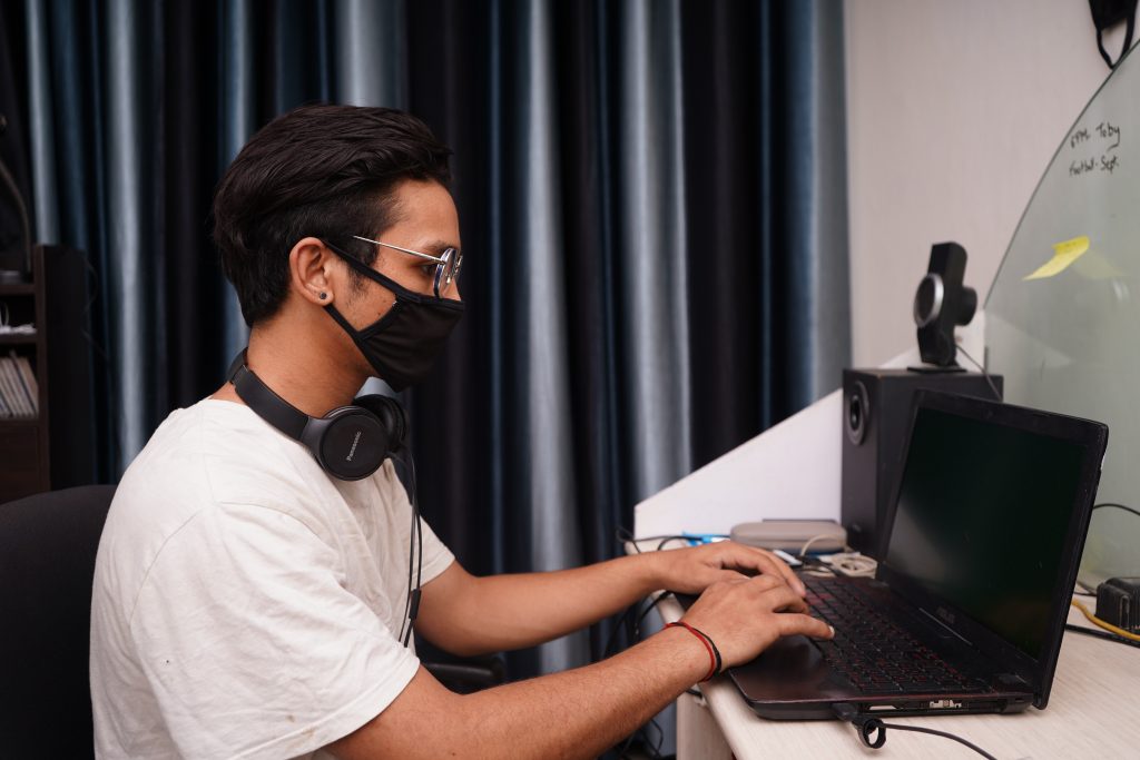 man with headphones and mask on working on the laptop