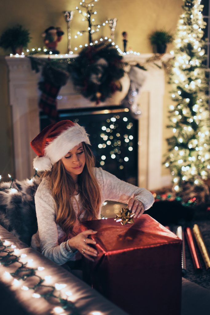 woman wearing a santa hat and placing a bow on present 
