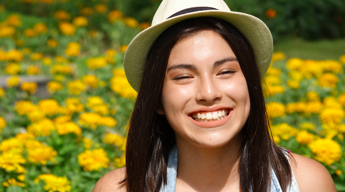 teen wearing blue top smiling in a field of flowers 