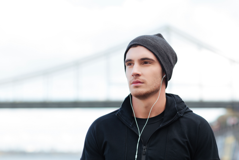 young man wearing headphones and a hat outdoors  