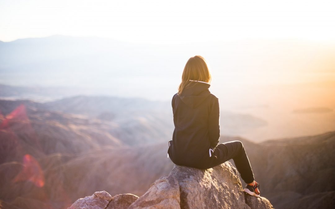 woman sitting on the edge of a mountain peak