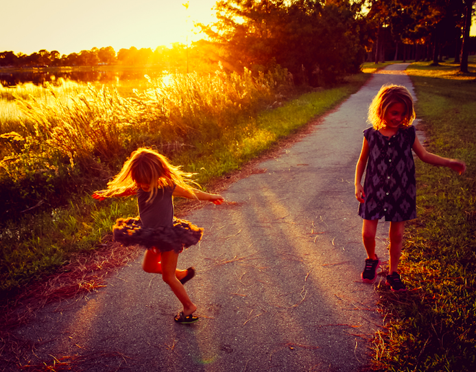 small girls playing happily on road with fields on both the sides