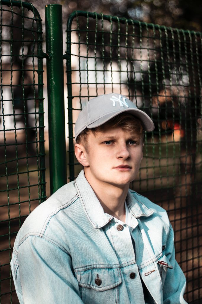 teen wearing a cap and  standing near the fence