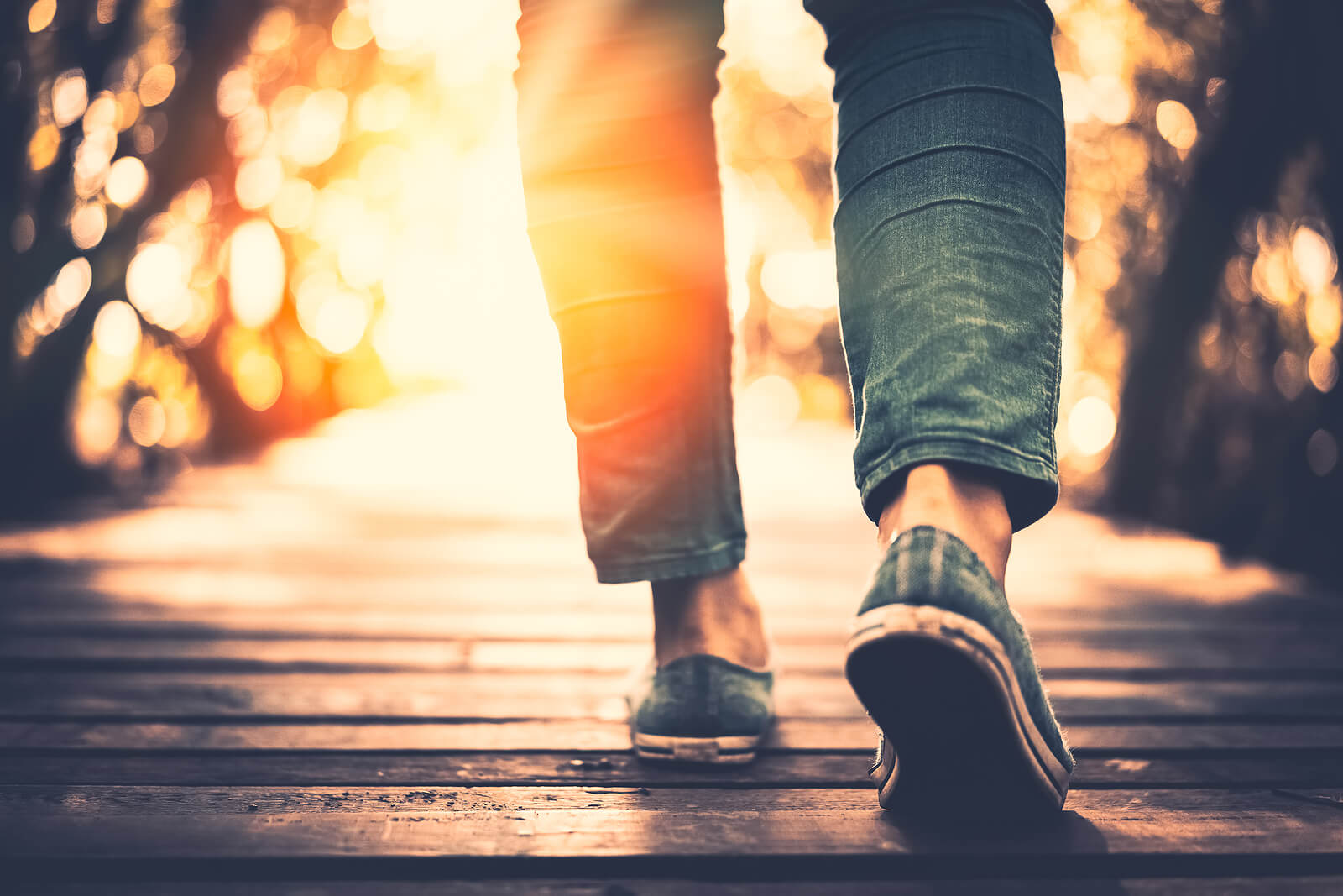 A close up of feet walking on a sunny path towards the rising sun. This could represent the brighter future trauma therapy in Simi Valley, CA can cultivate. Learn more about our services from a trauma therapist in Thousand Oaks, CA and other services. 93063
