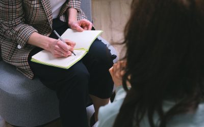 Counselor writing notes while talking to a patient during a session.