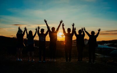 Group of people standing with their hands in the air watching the sunset.