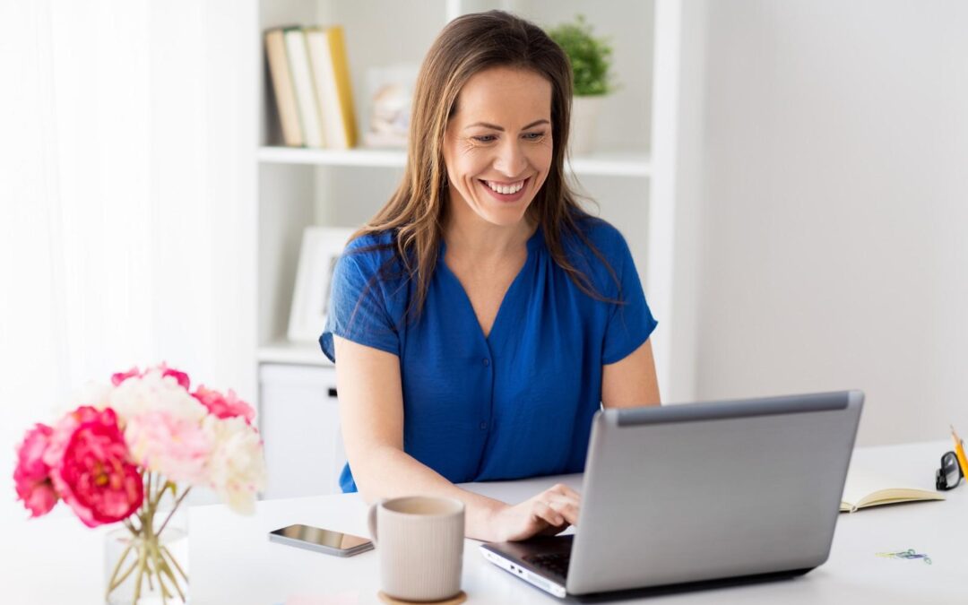 Woman in a blue blouse smiles at a laptop sitting in front of her
