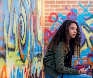 girl with long brown hair sits against a wall of graffiti