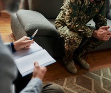 
A man sitting on a couch talking to a man in a military uniform.
