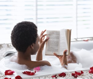 A woman reading a book in a bathtub with rose petals.