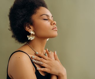 
A woman with afro hair and earrings is posing with her hands on her chest.