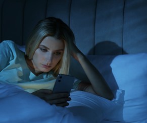 
A young woman looking at her phone in bed at night.