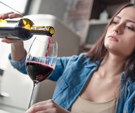 Woman in blue jacket pouring red wine into a glass