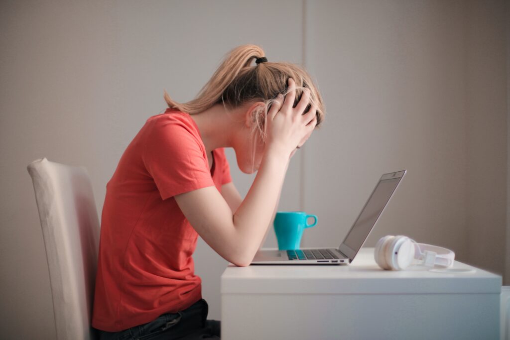 A woman holding her head looking at a laptop