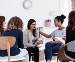 Group of women sat in a circle and talking in a white room
