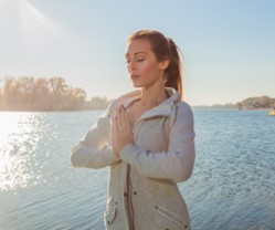 Woman standing near water with hands together