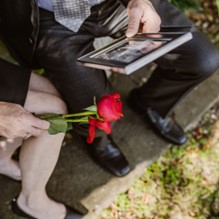 Man and woman sat on a concrete step holding roses and a photo frame