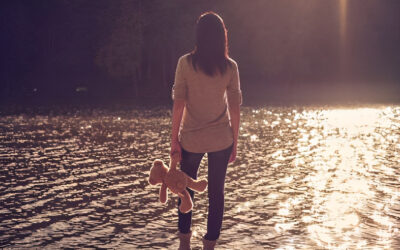 A woman is standing in the water holding a teddy bear.