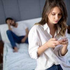 A woman looking at her phone while a man is sitting on the bed.