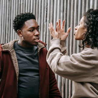 A man and woman are arguing in front of a wall.