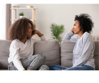 Two women talking on a couch at home.