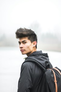 A young man with a backpack in front of a foggy lake.